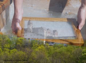 Hände halten einen Bilderrahmen, im Hintergrund Schlossmotiv