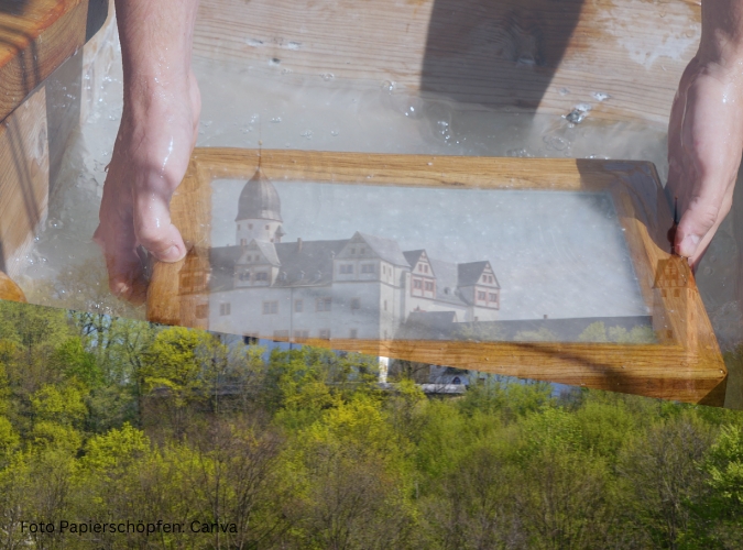Hände halten einen Bilderrahmen, im Hintergrund Schlossmotiv