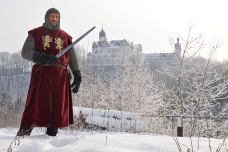 Das Bild zeigt einen Ritter. Im Hintergrund ist die verschneite Rochsburg zu sehen.