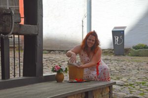 Brunnen Schloss Rochsburg, Gästeführerin Carmen Petrus am Brunnen sitzend, Kräuter in der Hand haltend