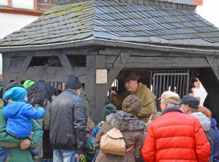 Gästeführer Michael Kreskowsky erklärt einer Gruppe Besucher den historischen Burgbrunnen auf Schloss Rochsburg. Kreskowsky ist historisch gewandet und hält einen Holzeimer in der Hand. Er lässt Wasser in den Brunnen tropfen und die Besucher lauschen gespannt, wie lange es dauert, bis das Wasser im Brunnen aufschlägt.