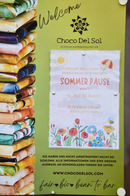 Im Bild sieht man einen Aushang der Schokoladenmanufaktur Choco Del Sol mit dem Hinweis auf deren Sommerpause vom 18. Juli bis 23. August 2026.